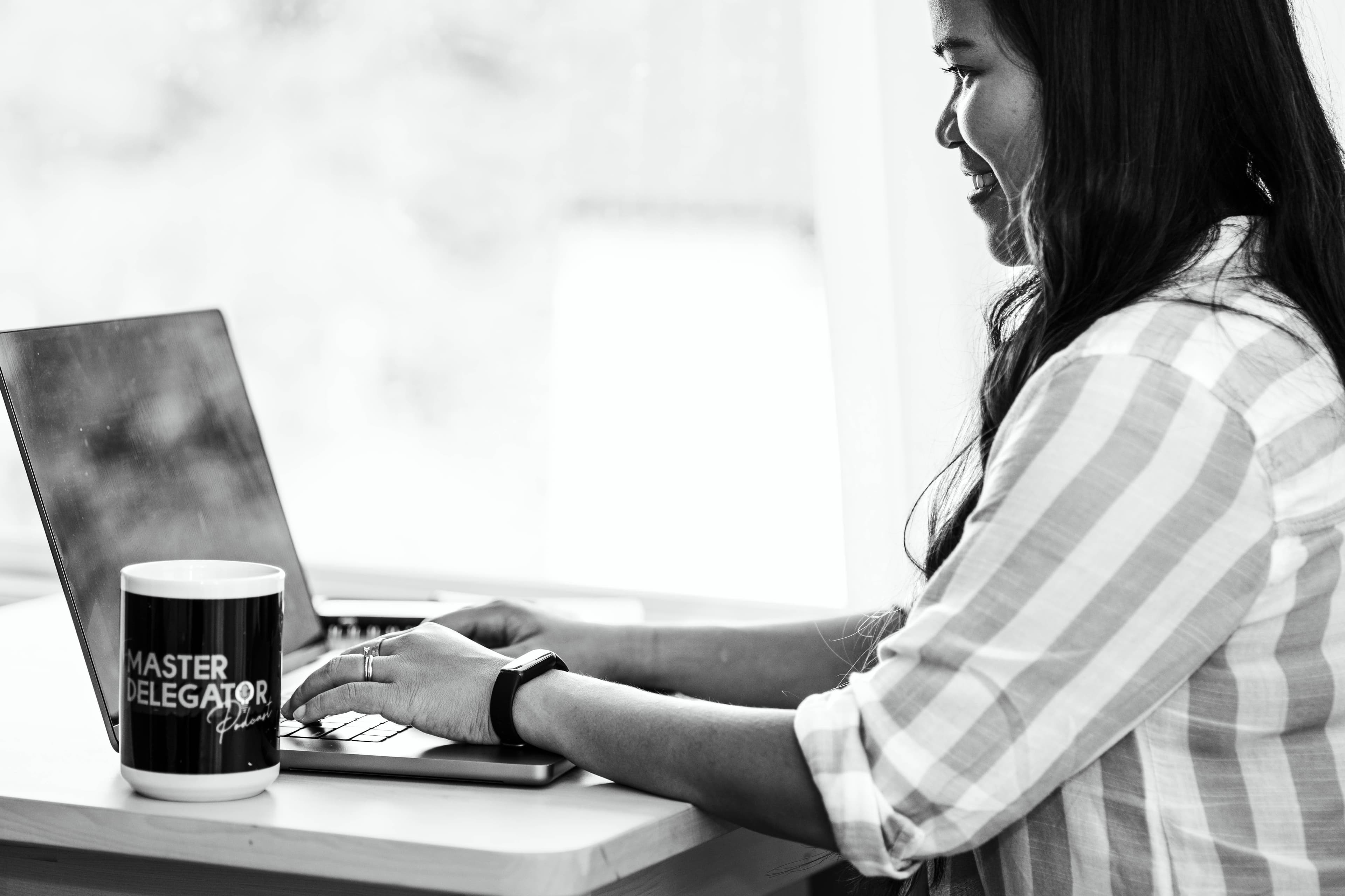 Kristy Yoder working at her laptop beside a Master Delegator mug, reflecting on letting go of control as a business owner