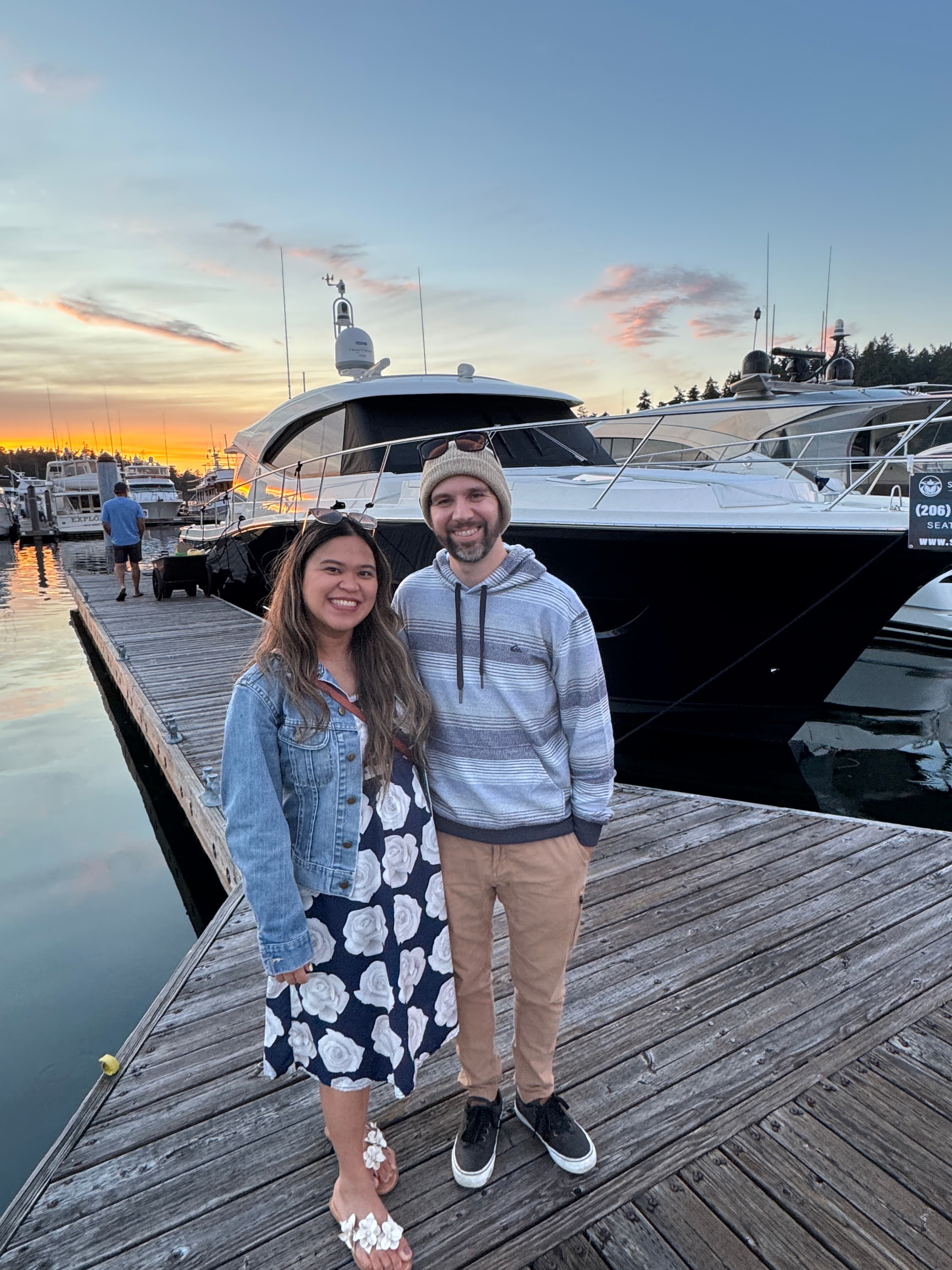 Kristy Yoder and her husband standing on a marina dock at sunset in front of a docked yacht